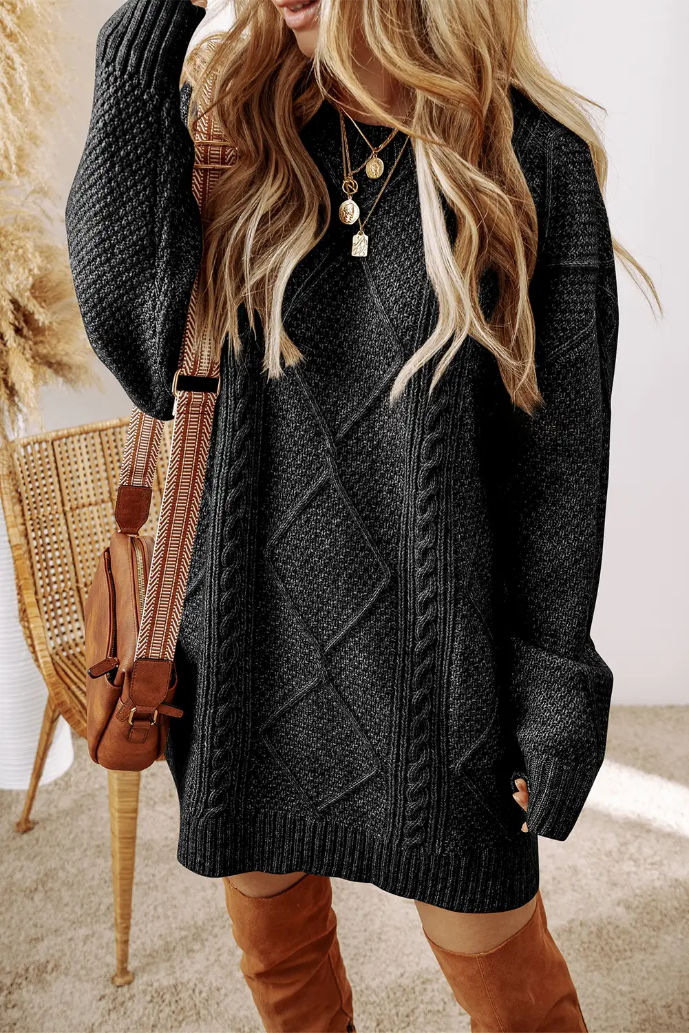 Woman in a black cable knit sweater dress, relaxed in natural window light